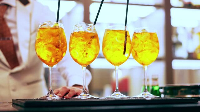 Refreshing Aperol Spritz cocktail glasses with black drinking straws at the bar counter, vibrant colours of fizzing beverage, bartender preparing cocktails for guests