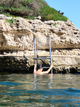 Swimmer using ladder to exit turquoise water in Menorca