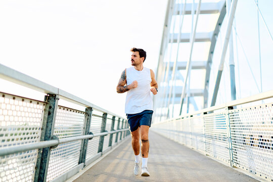 Athletic man running outdoors on a modern bridge, engaging in an urban workout for active lifestyle and health