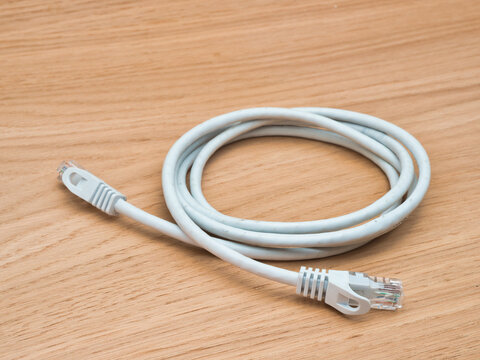 White Ethernet Cable on Wood Surface - A white coiled Ethernet patch cord with RJ45 connectors is placed on a light brown wooden tabletop, ready for network connectivity.