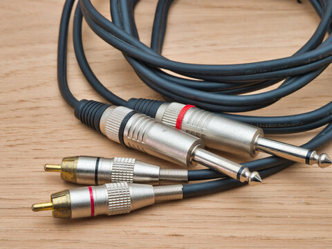 Audio Cable with Jack and RCA Plugs - A black audio cable featuring both 1/4 inch jack and RCA phono connectors rests on a light wooden background.