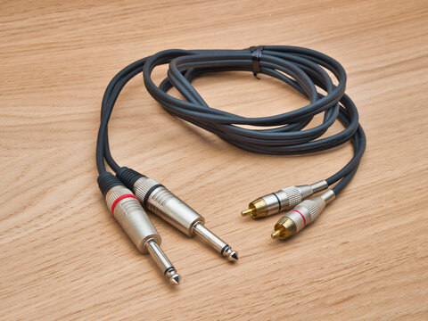 Audio Cable with Jack and RCA Plugs - A black audio cable featuring both 1/4 inch jack and RCA phono connectors rests on a light wooden background.