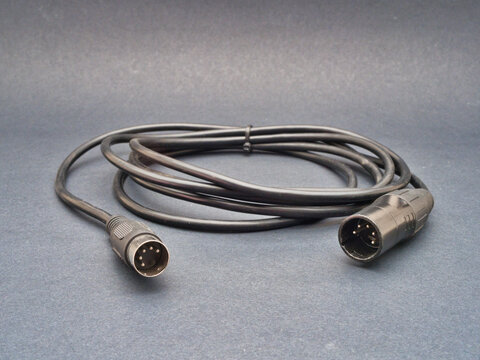 Black Audio Cable with XLR and DIN Conne - A black audio cable with a 5-pin DIN connector and a 3-pin XLR connector lies coiled on a dark grey surface, ready for use.