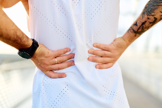 Man holding his lower back, experiencing sharp pain and discomfort during or after physical activity or training outdoors
