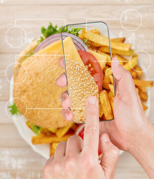Hands hold a phone over a burger and fries to log nutrition