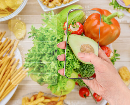 Hand scans healthy produce on a phone beside chips and fries