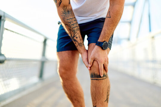 Athlete feeling joint pain in his knee during an outdoor workout. Concept of sports injury, healthcare, and active lifestyle