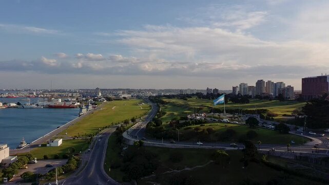 Bandera argentina flameando frente a la costa y el puerto de una ciudad argentina, vista a&eacute;rea