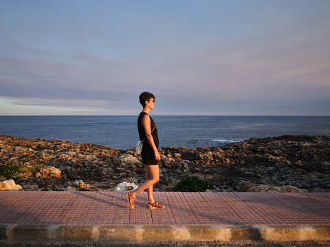 Woman walking along Menorca coast at sunset