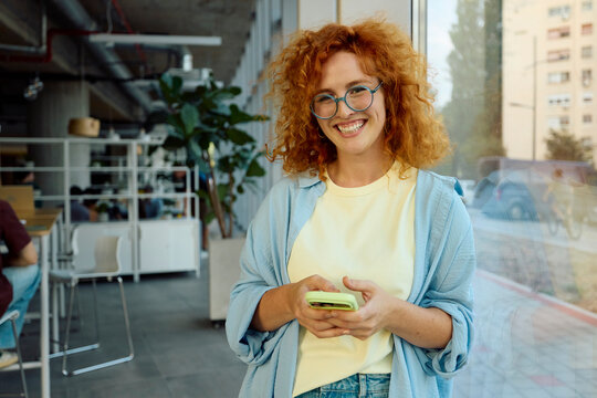 Young woman smiles while holds her phone in a shared workspace