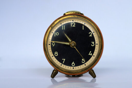 Ein alter analoger rot-goldener Wecker mit hellem, neutralen Hintergrund