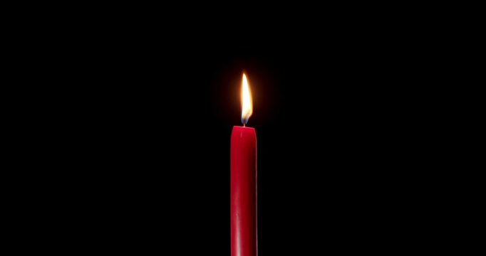 A single red candle burning on a black background. The bright flame of this isolated candle shines in the dark. A peaceful candle ideal for holiday celebration, memory, or spiritual concept.
