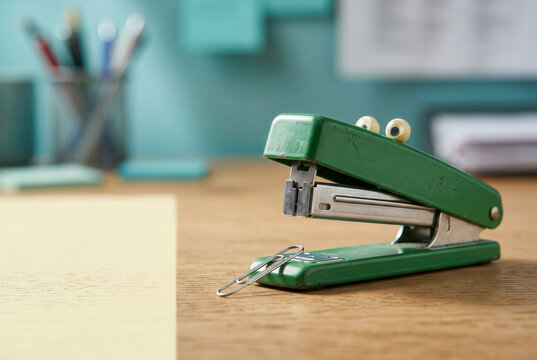 Green Stapler with Googly Eyes on a Wooden Desk