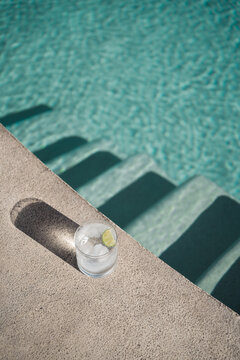 transparent drink in a glass with ice and lime by the pool