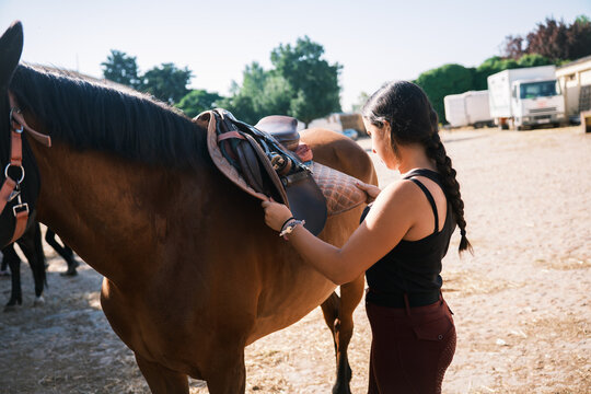 Horsewoman putting the saddle on the horse