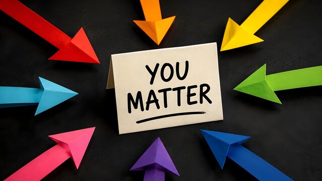 You matter handwritten message on paper card surrounded by colorful origami pointing arrows on dark background. Positive motivation and mental health affirmation concept.
