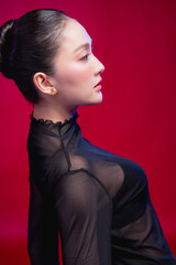 A striking profile portrait capturing the elegant lines of a woman's face and neck, sleek high bun and sheer black fabric against a deep red backdrop, pure sculptural beauty. © whyframeshot