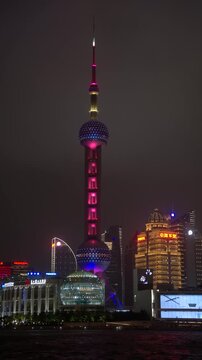 SHANGHAI, CHINA - AUGUST 23, 2026: Oriental Pearl Tower glows with colorful LED lights over the riverfront skyline at night in SHANGHAI CHINA, in vertical timelapse