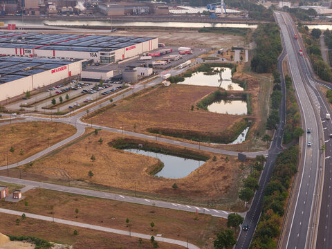 Genk, Belgium - 27 August 2026: Aerial view of Genk-Zuid Rechteroever industrial site with warehouses, stormwater management infiltration basins, and highway infrastructure.