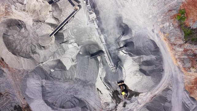 Drone view of gravel conveyor system with dust cloud. Overhead shot of stone crusher belts, stockpiles and a loader working the quarry floor.