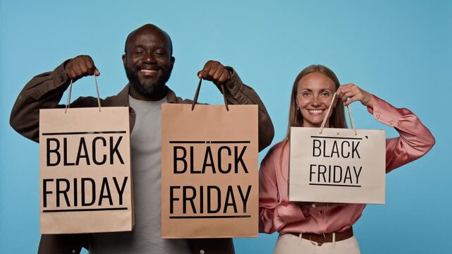 Portrait of smiling African American man and Caucasian woman raising Black Friday shopping bags. Video suited for retail sales promotions, discount advertising and marketing campaigns