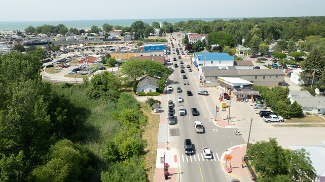 Caseville, Michigan, United States - 04 July 2025: Aerial view of the main street in Caseville, featuring local businesses, parked cars, trees, and the nearby lake.