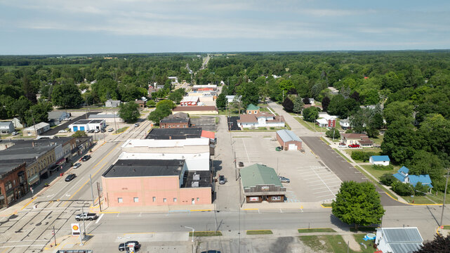 Carson City, Michigan, United States - 28 June 2025: Aerial view of the town center featuring local businesses, parking lots, and surrounding green trees under a clear blue sky.