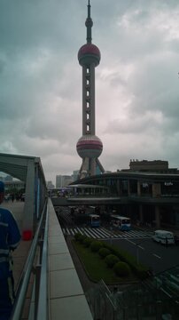 SHANGHAI, CHINA - AUGUST 23, 2026: Camera tilts up to the full height of Oriental Pearl Tower over Lujiazui pedestrian bridge on a cloudy day in SHANGHAI CHINA, in timelapse