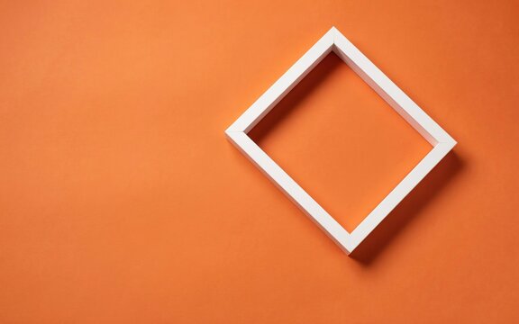 A single white square frame tilted at an angle on a plain orange background, creating a minimalist and clean geometric composition