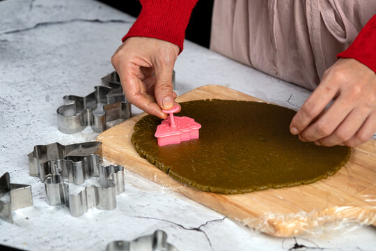 Hands cutting rolled dough with pink cookie cutter on wooden board, surrounded by metal cutters for baking, pastry preparation, homemade cookies and festive kitchen cooking