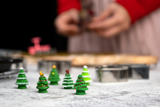 Christmas tree decorations in foreground with baking tools, cookie cutters and blurred hands behind, festive holiday preparation, seasonal cooking, craft and celebration concept