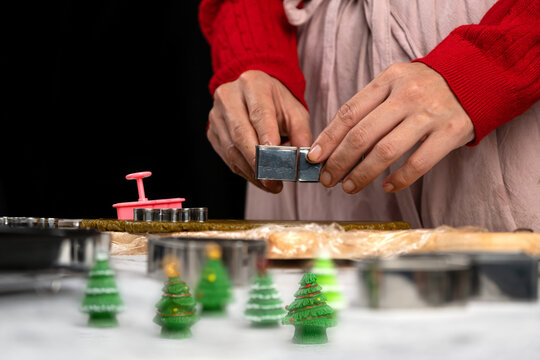 Hands shaping festive cookie dough with metal cutter beside Christmas tree decorations, baking preparation, holiday cooking, homemade pastry and seasonal kitchen tradition