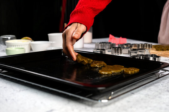 Hand arranging homemade cookies on baking tray beside metal cutters, festive holiday baking, pastry preparation, Christmas cooking, dessert making and seasonal kitchen tradition