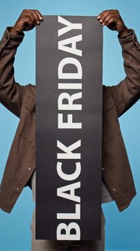 Portrait of African American man raising Black Friday banner against blue background. Perfect for holiday shopping promos and seasonal retail sales campaigns, vertical