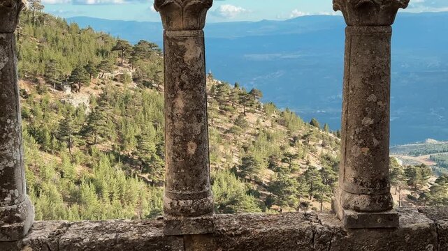 Ancient stone columns, decorative capitals and arches at Alahan Monastery in Mut, with a hazy mountain landscape visible in the distance.