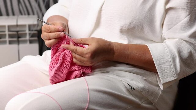 Woman crochets bag made of knitted pink threads. Engaging hobby