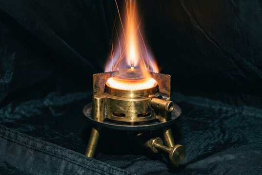 Brass camping burner with flame on dark fabric background
