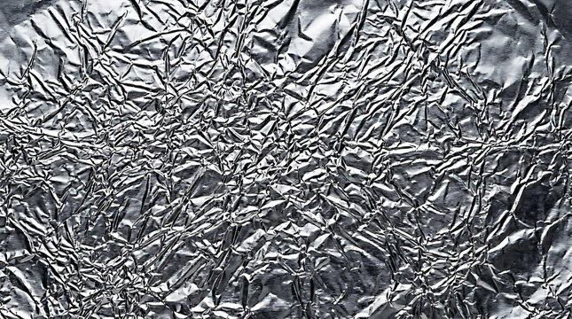 Abstract background of crumpled silver aluminum foil with deep shadows and bright highlights creating a metallic texture