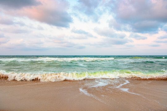 golden cloudy evening above the green sea waters. waves crashing the sandy beach. clear horizon. changing windy weather. dramatic sky