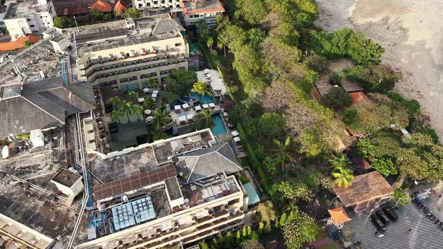 Aerial photo of Sunrise Hotel in Seminyak, Bali showing rooftop structures, central pool courtyard, lush tropical gardens and the adjacent sandy beach, evoking travel, relaxation and coastal resort