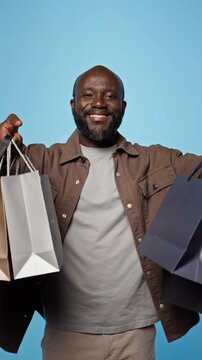 Portrait of smiling African American man raising shopping bags. Perfect for e-commerce marketing, retail sales campaigns and holiday shopping promotions, vertical
