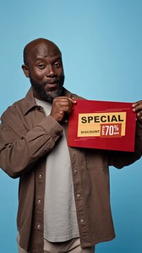 Portrait of African American man holding discount sign, showing excitement. Clip suitable for retail marketing campaigns, ecommerce promo, seasonal store sale advertisements, vertical