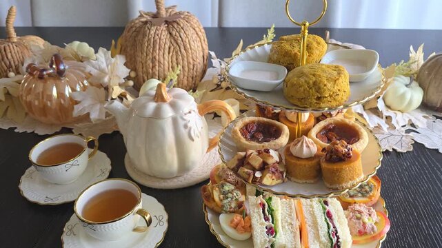 Autumn theme afternoon tea table scene with pumpkin spice tea, scones, cozy pumpkin, pecan and apple desserts and fall theme finger sandwiches and savory items. Slow downward panning motion.