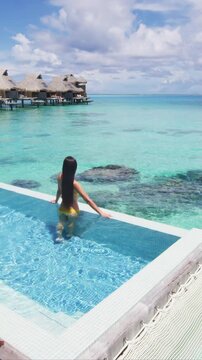Luxury resort travel vacation destination idyllic overwater bungalow villa woman relaxing by infinity pool. Social media influencer traveler luxurious lifestyle. Raw vertical video of real woman.