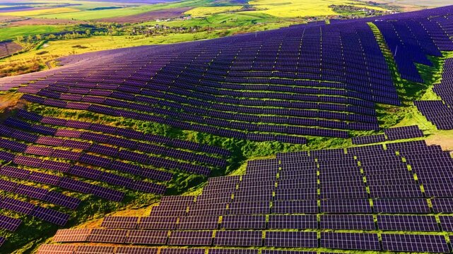 Morning light glows across solar panel hillside, Bulgaria. Elevated shot reveals nearby village, winding path and patchwork farmland beyond.