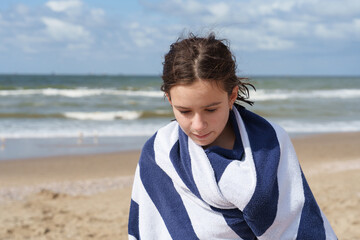 Teen girl wrapped in beach towel looking down by windy sea © EkaZehner