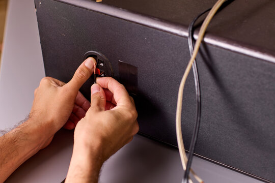 Close-up of hands plugging audio cable into speaker jack with visible fingertip grip