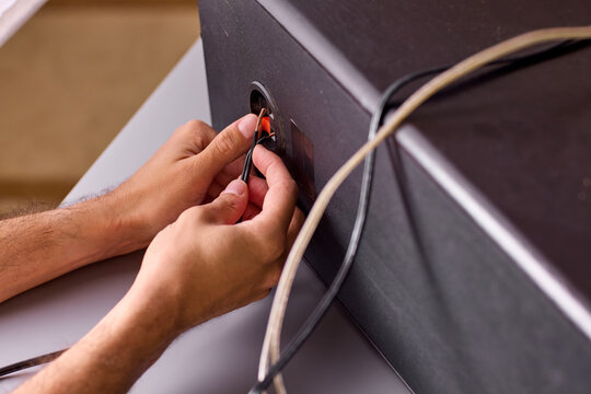 Close-up of hands plugging audio cable into speaker jack with visible fingertip grip