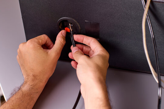 Close-up of hands plugging audio cable into speaker jack with visible fingertip grip
