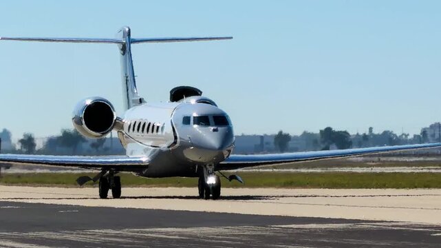 A private jet taxis toward the viewer in afternoon light.  The jet shines with reflected sunlight and moves from the distance to very close up.